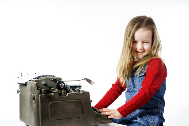 Cute little girl typing on vintage typewriter keyboard - Фото, изображение