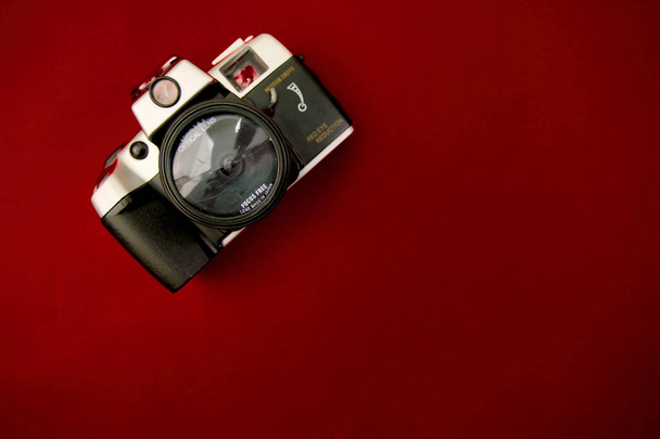 A high-resolution image featuring a vintage camera positioned flat against a solid red surface - Zdjęcie, obraz