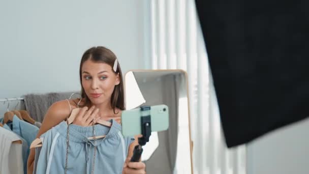 Νεαρή γυναίκα δημιουργός περιεχομένου κοινωνικών μέσων κάνει βίντεο μόδας. Blogger χαμογελά στην κάμερα χρησιμοποιώντας selfie ραβδί και ελαφρύ δαχτυλίδι, ενώ κάνοντας πειστική σε απευθείας σύνδεση ρούχα πωλούν vlog στο κοινό ή οπαδός. Διεύθυνση - Πλάνα, βίντεο