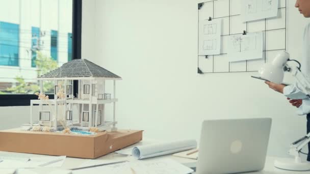 Professionele knappe Aziatische project manager met behulp van tablet om huismodel te controleren terwijl inspecteren huis model structuur zorgvuldig op kantoor met blauwdruk gestript achter. Creatief ontwerp. Onbevlekt. - Video