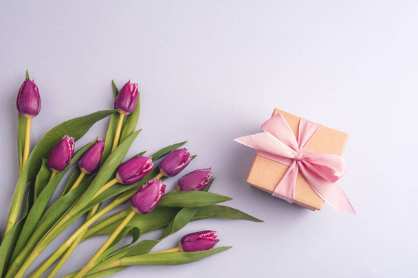 Tulipanes rosados y regalo en una caja sobre fondo morado. Concepto vacaciones de primavera. Vista superior, plano. - Foto, imagen
