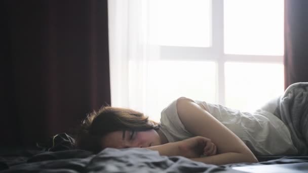 Девушка в пижаме спит в спальне рядом со своим ноутбуком, большое окно на заднем плане. Медленное движение. Работа дома, концепция образа жизни - Кадры, видео