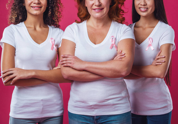 Nők, mellrák ellen. Gyönyörű nők különböző korú és nemzetiségű rózsaszín szalag-ra-uk ládák mosolyogva, vágott, piros háttér - Fotó, kép