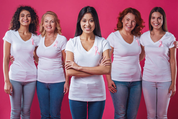 Kobiety z rakiem piersi. Piękne kobiety w różnym wieku i narodowości z różowe kokardki na ich skrzynie są uśmiechnięte, na czerwonym tle - Zdjęcie, obraz