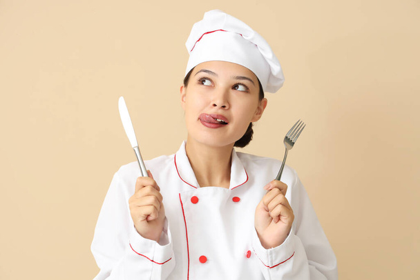 Женский азиатский шеф-повар со столовыми приборами на бежевом фоне - Фото, изображение