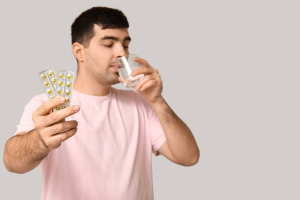Young man with blisters of vitamin A pills drinking water on light background, closeup - Photo, Image