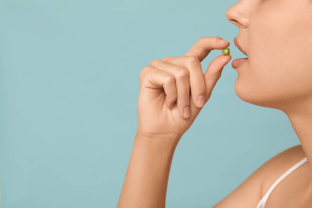 Hezká mladá žena užívat vitamin A kapsle na modrém pozadí, detailní záběr - Fotografie, Obrázek