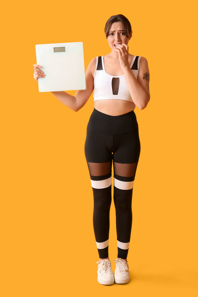 黄色の背景にスケールを持つ美しい心配した女性. 減量コンセプト - 写真・画像