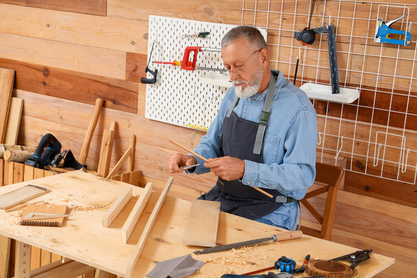 Carpinteiro maduro trabalhando com prancha de madeira à mesa na loja - Foto, Imagem