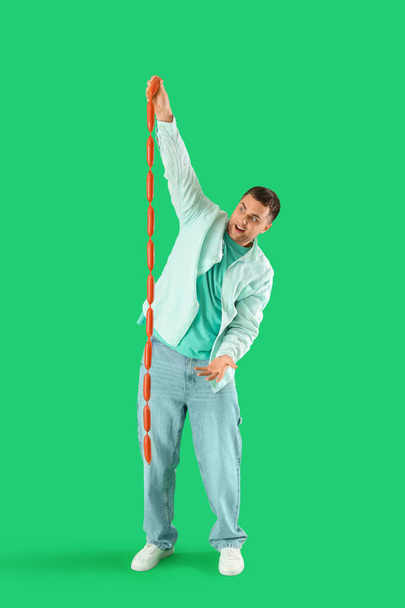 Vrolijke jongeman met lekkere worstjes op groene achtergrond - Foto, afbeelding