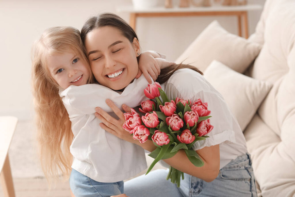 Kleines Mädchen gratuliert ihrer Mutter zu Hause mit einem Blumenstrauß. Muttertagsfeier - Foto, Bild