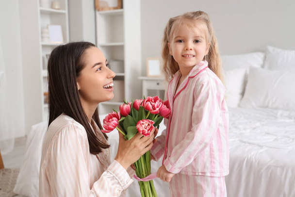 Маленька дівчинка вітає свою щасливу маму з букетом красивих квітів у спальні. Святкування Дня матері - Фото, зображення