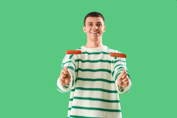 Fiatal férfi ízletes kolbászok zöld háttér - Fotó, kép