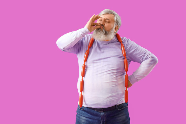 Mature man with tasty sausages on purple background - Photo, Image