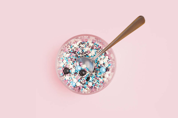 Vidrio y cuchara con chispas de colores dulces sobre fondo rosa - Foto, Imagen