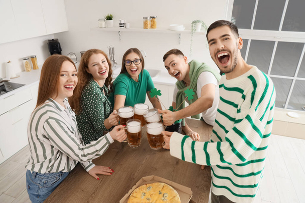 Группа молодых друзей с пивом и пиццей празднуют День Святого Патрика на кухне - Фото, изображение