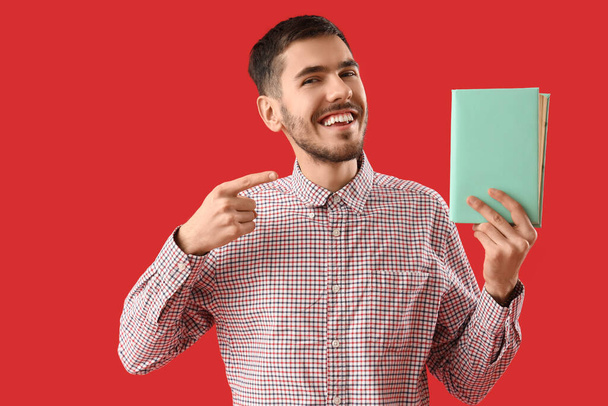 Mladý muž ukazuje na knihu na červeném pozadí - Fotografie, Obrázek