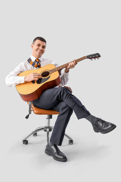 Hombre de negocios divertido tocando la guitarra en la silla de la oficina sobre fondo claro - Foto, Imagen