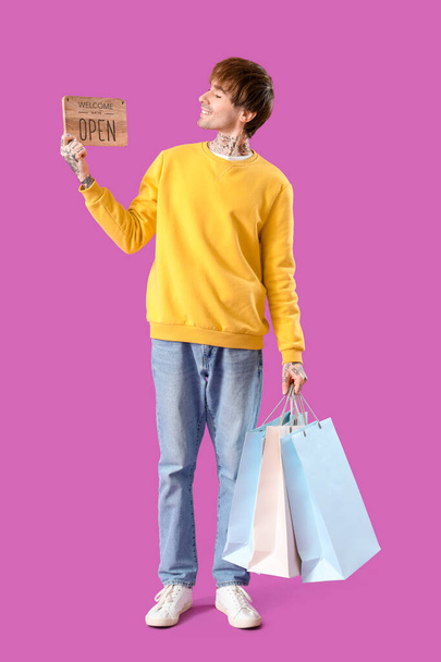 Nuori verkkokaupan myyjä maksupäätteellä ja ostoskassit violetti tausta - Valokuva, kuva
