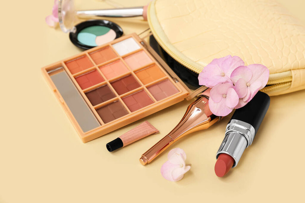 Kozmetikai táska smink termékek szemek, rúzs és virágok világossárga háttér, közelkép - Fotó, kép
