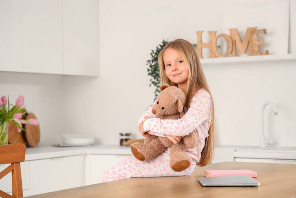 schattig klein meisje met speelgoed beer in keuken - Foto, afbeelding