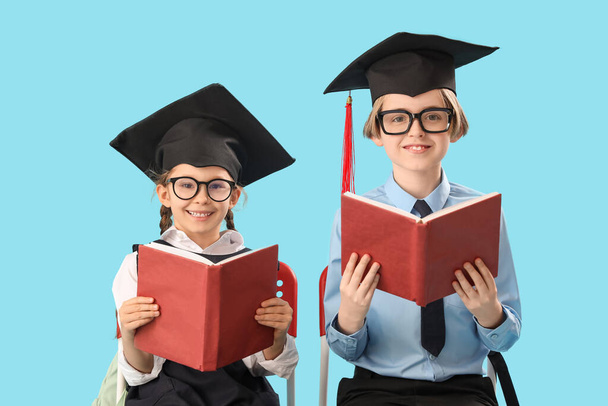 Niños pequeños con sombreros de graduación leyendo libros sobre fondo azul. Fin del año escolar - Foto, imagen