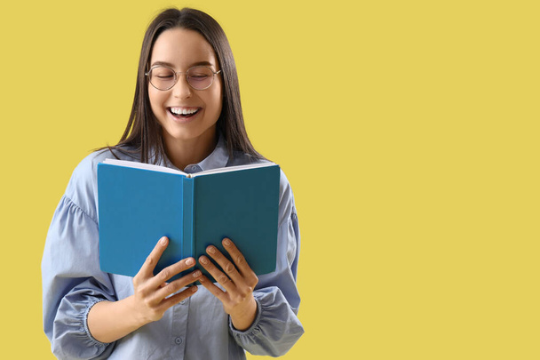 Mosolygó fiatal nő olvasás könyv sárga háttér - Fotó, kép