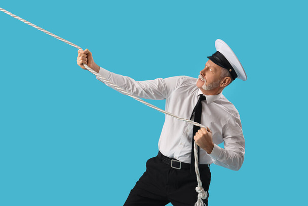marinaio maturo tirando corda su sfondo blu - Foto, immagini