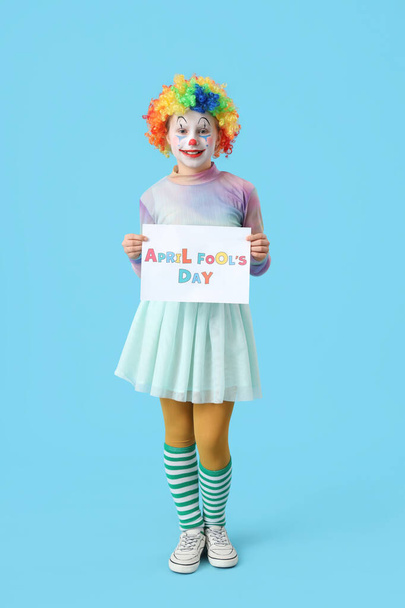 Funny little girl in clown wig with card on blue background. April Fools' Day celebration - Photo, Image