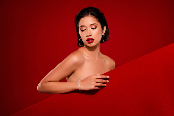 Photo of gorgeous korean young lady sexy look down behind empty space shoulders off isolated on red color background. - Photo, Image