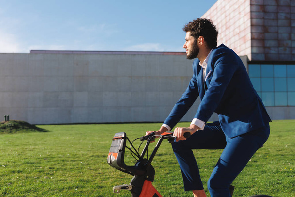 Schöner hispanischer Millennial-Geschäftsmann auf einem Fahrrad im modernen Park. Hochwertiges Foto - Foto, Bild