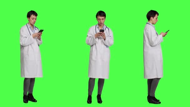 İnsanlara mesaj atmak için sosyal medya uygulamalarında gezinen bir doktor yeşil perde arkaplanına karşı duruyor. Beyaz önlüklü doktor internet sitelerine girip randevu alıyor. Kamera A. - Video, Çekim