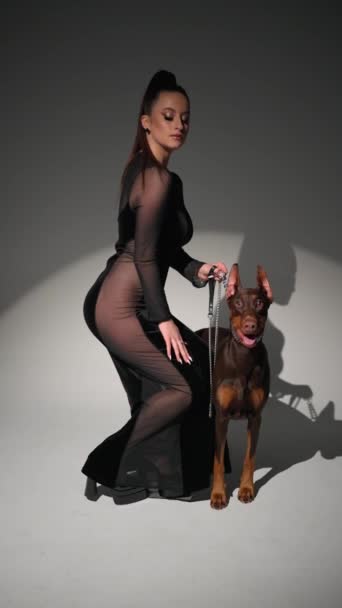 Model in transparent dress leads doberman on leash in studio. - Footage, Video