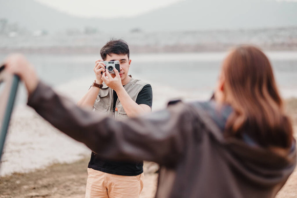 À travers la lentille de son appareil photo, un jeune homme se concentre sur la prise d'un portrait d'une personne avec le lac serein comme toile de fond. - Photo, image