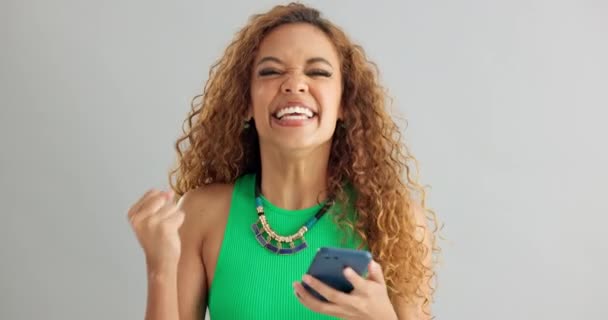 Excited woman, winner and phone with good news for lottery, prize or promotion on a gray studio background. Happy female person dancing with smile and mobile smartphone for celebration or success. - Footage, Video
