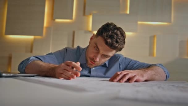 Professional builder writing draft in modern architectural agency close up. Serious smart architect working on construction blueprint at office. Unshaven engineer looking on building plan making notes - Footage, Video