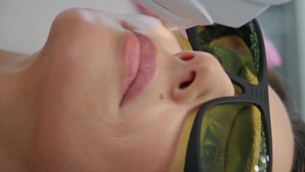 Unknown professional cosmetician making laser procedure to attractive woman client vertically close up. Lady in protective glasses having hardware skin wrinkles correction. Beauty salon therapy - Footage, Video