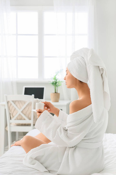 Giovane donna con asciugamano e tazza di caffè dopo la doccia in camera da letto, vista posteriore - Foto, immagini