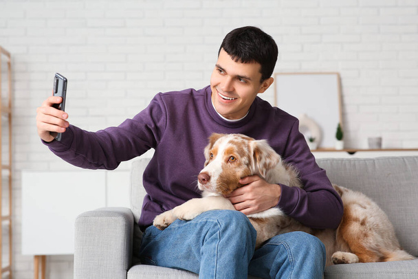 Young man with Australian Shepherd dog taking selfie on sofa at home - Photo, Image
