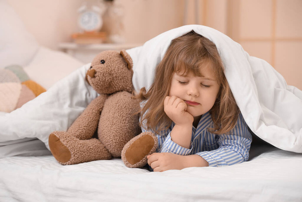 Αξιολάτρευτο κοριτσάκι με αρκουδάκι να κοιμάται κάτω από κουβέρτα στο κρεβάτι. - Φωτογραφία, εικόνα