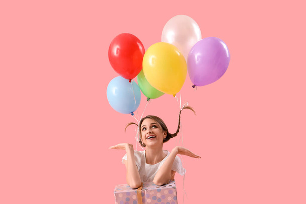 Молода жінка з повітряними кулями та подарунковою коробкою на рожевому фоні - Фото, зображення