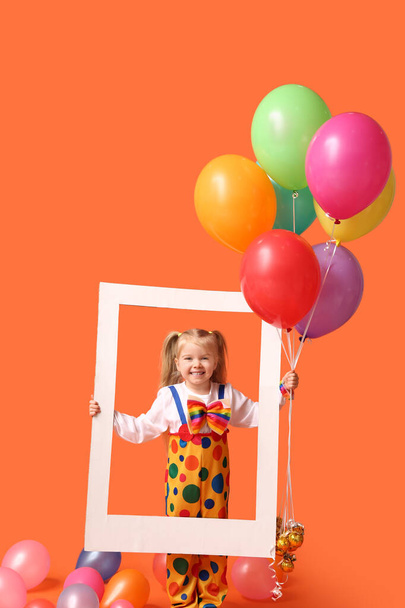 オレンジ色の背景に風船とフレームでピエロの衣装で笑う小さな女の子 - 写真・画像