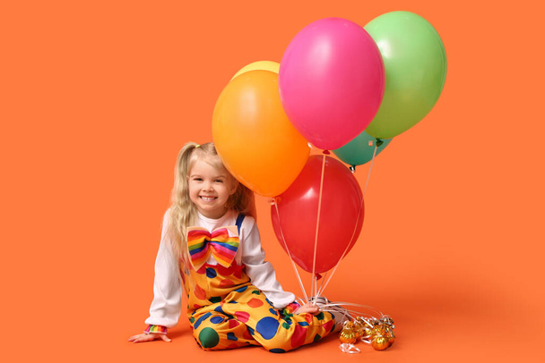Lachend klein meisje in clownspak met ballonnen op oranje achtergrond - Foto, afbeelding