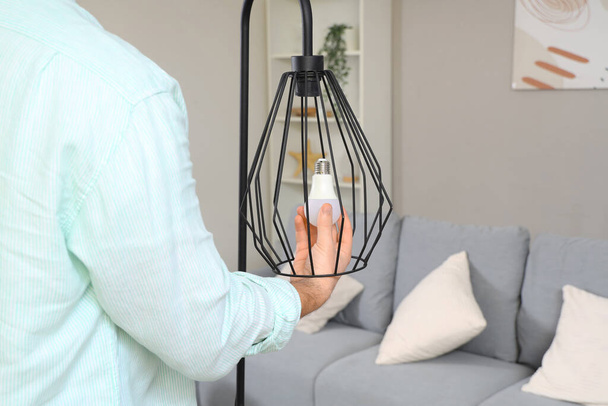 Молодий чоловік міняє лампочку в стандартній лампі вдома, крупним планом - Фото, зображення