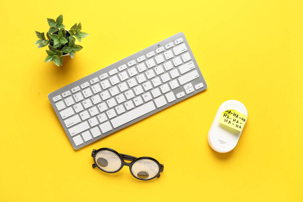 Funny glasses, sticky note, computer keyboard and mouse on yellow background. April Fools Day prank - Photo, Image