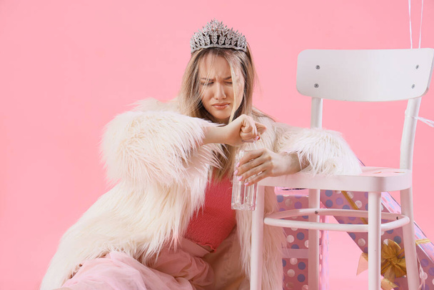 Jonge vrouw met kater en water fles na verjaardag feest op roze achtergrond - Foto, afbeelding