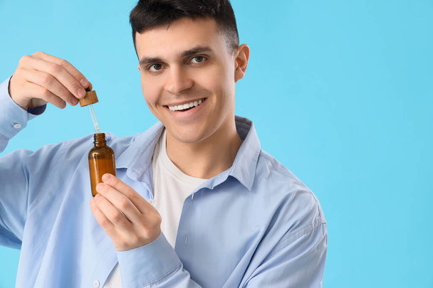 Young man with bottle of CBD oil on blue background - Photo, Image