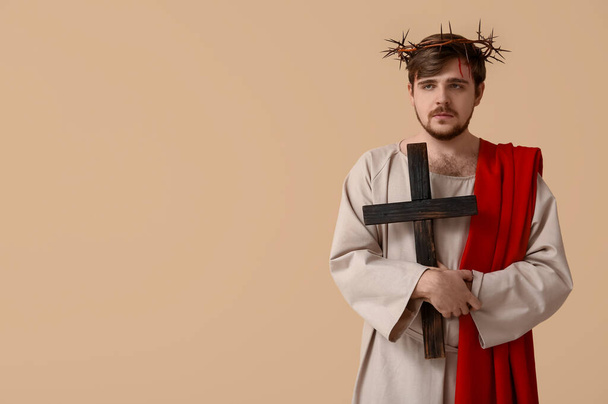 Uomo in veste di Gesù e corona di spine con sangue che regge croce di legno su sfondo beige - Foto, immagini