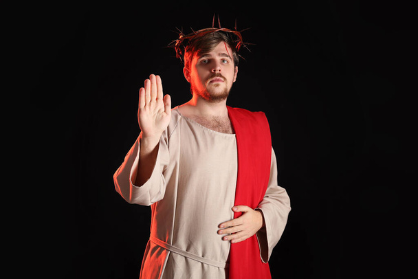 Ο άνθρωπος με τη ρόμπα του Ιησού και το στεφάνι από αγκάθια δείχνει σήμα στοπ με κόκκινο φως σε μαύρο φόντο - Φωτογραφία, εικόνα