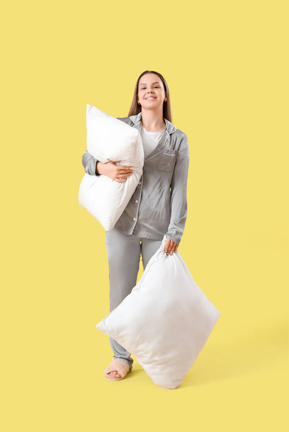 Νεαρή γυναίκα με πιτζάμες με μαλακά μαξιλάρια σε κίτρινο φόντο - Φωτογραφία, εικόνα